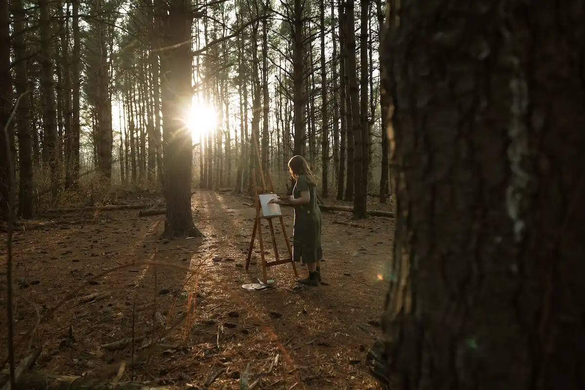 Artist painting at an easel in a sunlit pine forest