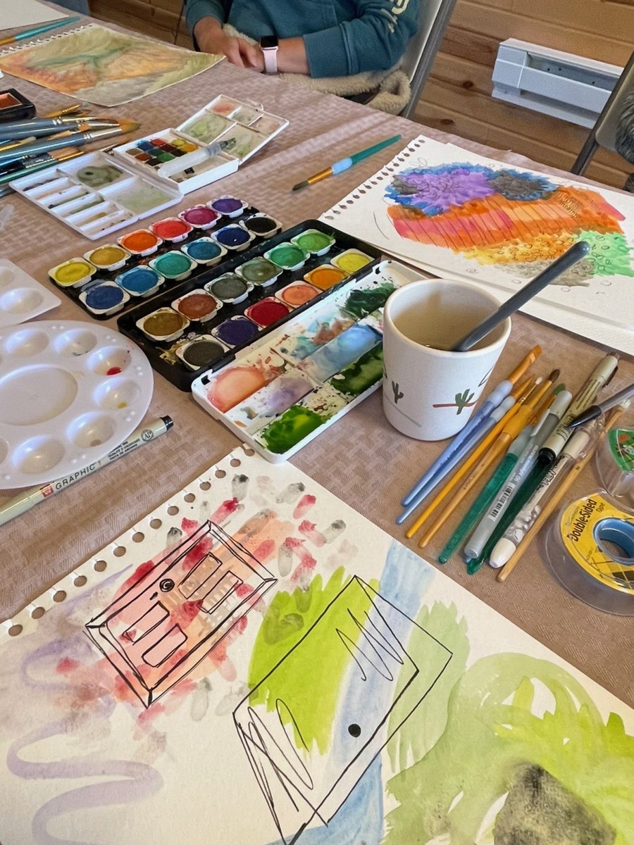 A senior living resident painting watercolors at a table set with palettes, brushes, and finished work